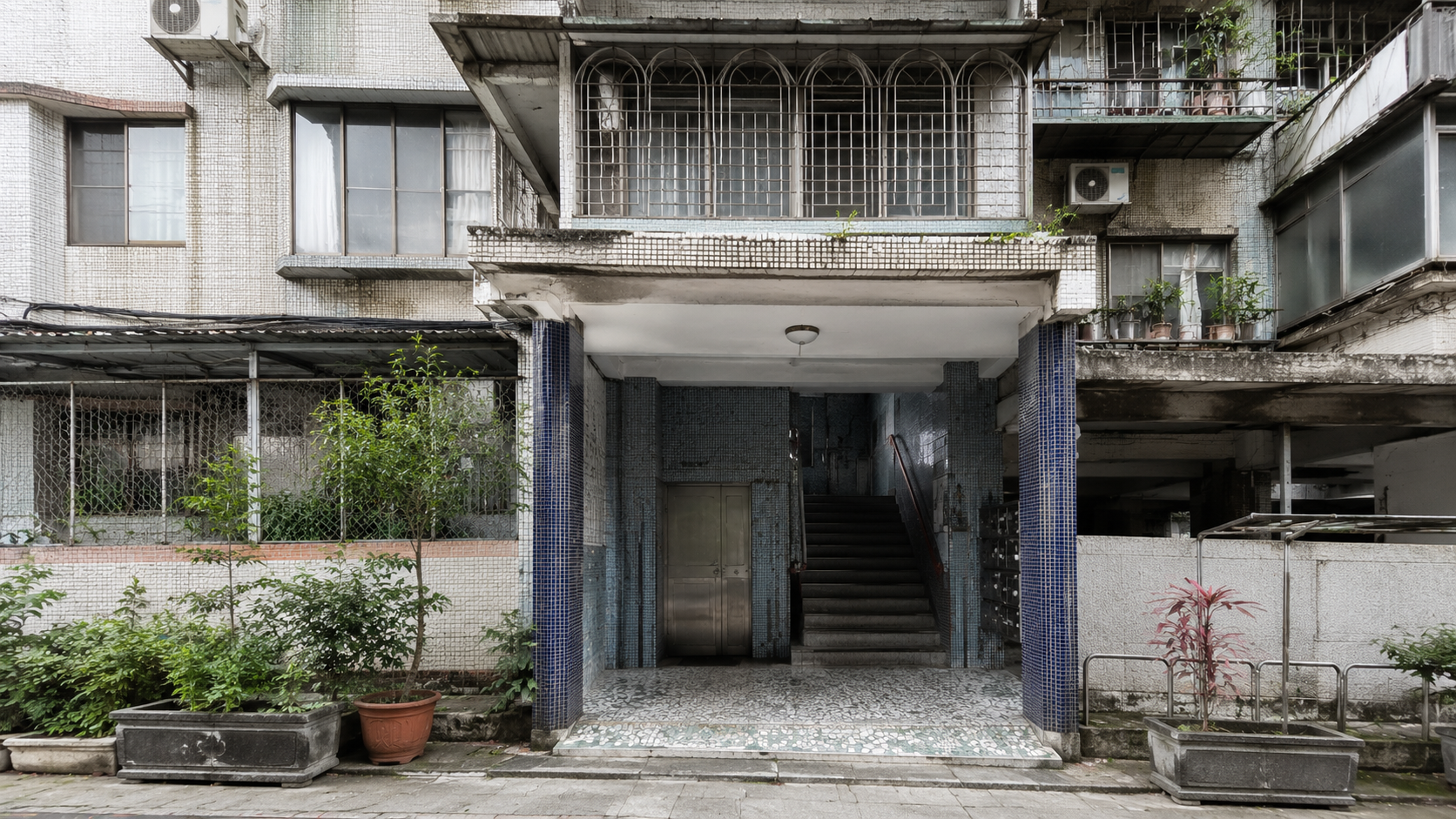 台灣老公寓入口與外觀現況照片，可見建築老化痕跡、公共空間與外部管線，呈現老屋修繕前的住宅狀態。